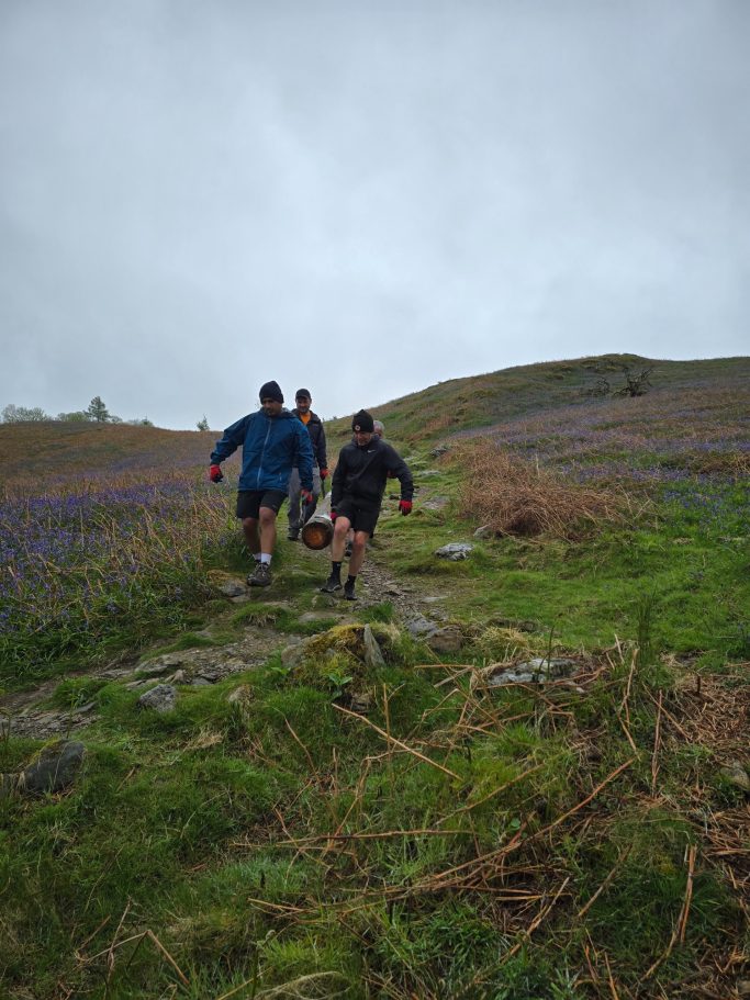 Three people walking on a rocky path through a hilly landscape with purple flowers.