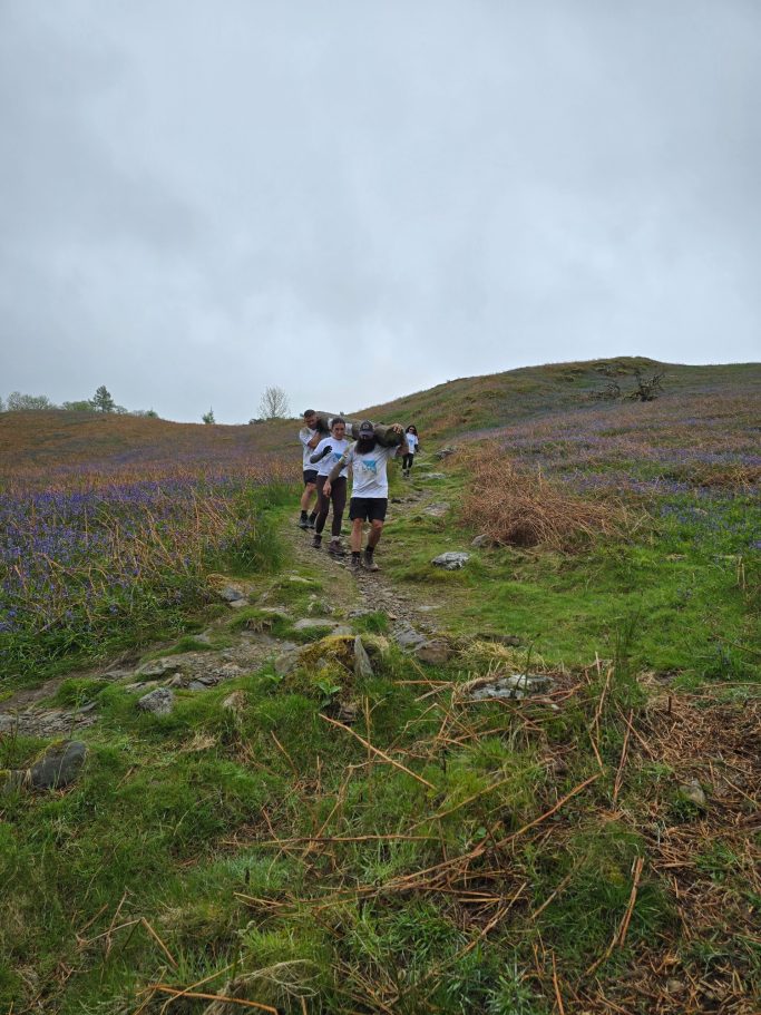 Two hikers walking along a narrow path through a grassy and flower-filled landscape.