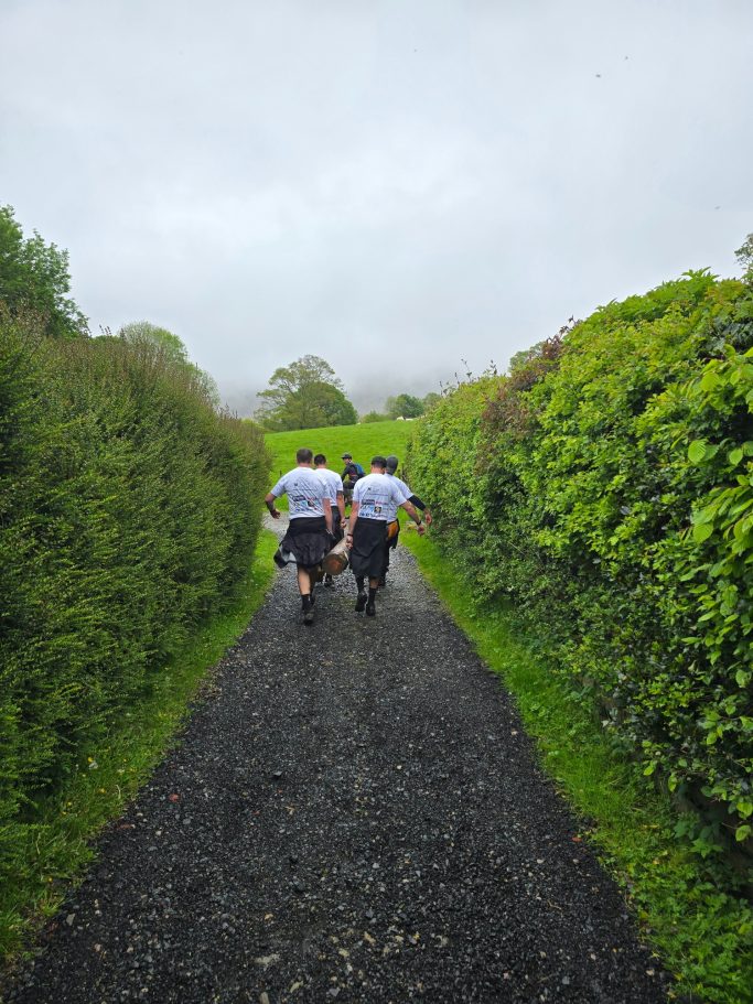 Two people walking down a gravel path between hedges on a cloudy day.