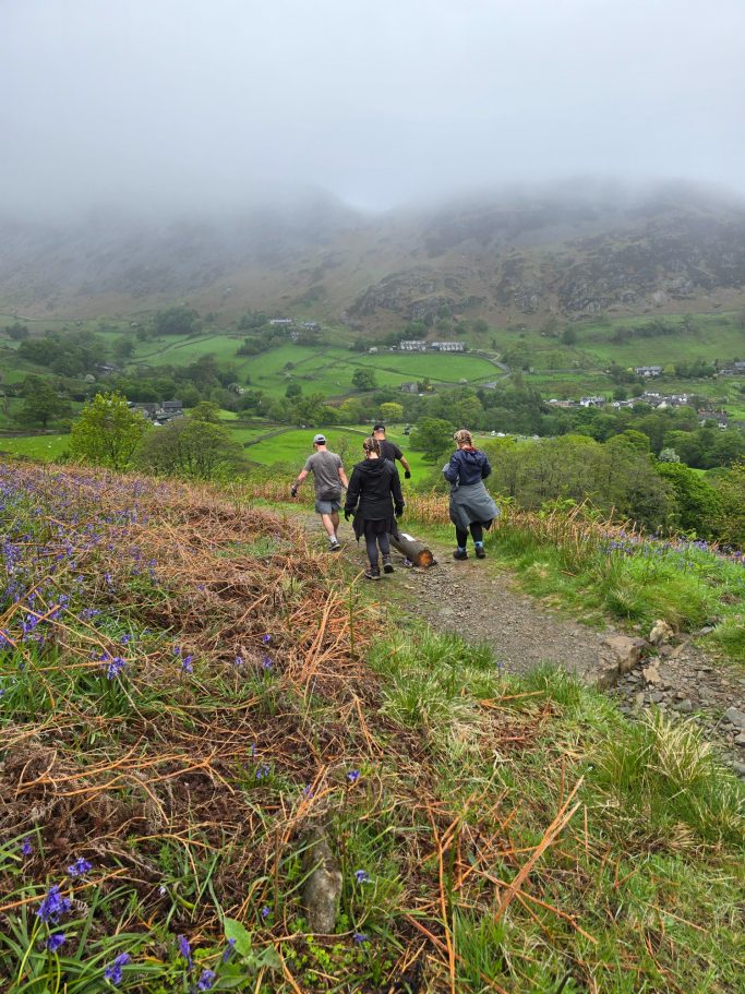 Three hikers walking down a path in a misty landscape with hills and greenery.